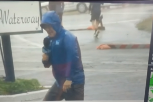 Seorang Reporter Secara Dramatis Bertahan dari Angin Badai Saat Membawakan Berita, Dan 2 Orang Pria Berjalan Santai Di Belakangnya